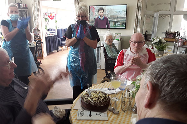 Silverpoint Court Residential Care Home resident smiling at the camera with his chocolate birthday cake as staff and residents give him a round of applause
